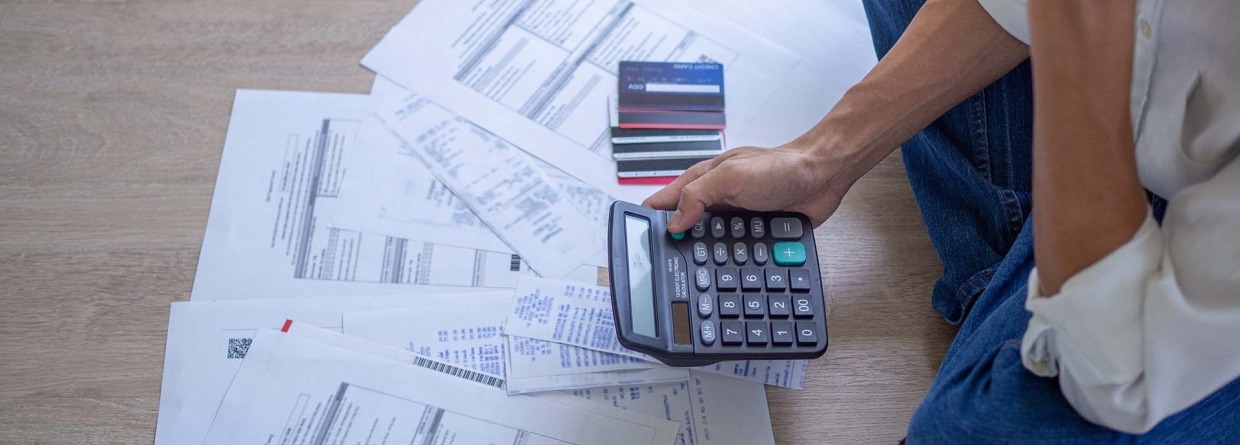 Man met stress zit op de grond met allemaal rekeningen, creditcards en een rekenmachine