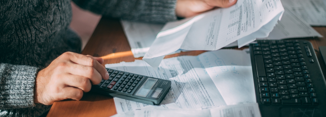 Een man achter een bureau met facturen op zijn bureau en een factuur in zijn hand maakt hij een berekening op zijn rekenmachine