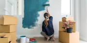 Vrouw schildert een muur blauw van een kamer met dozen op de achtergrond